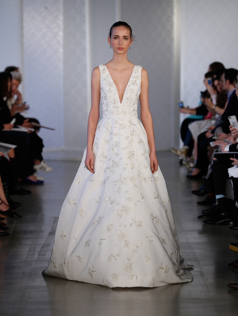 A model walks the runway at Oscar de la Renta Bridal’s spring 2017 show wearing an embellished gown with plunging neckline