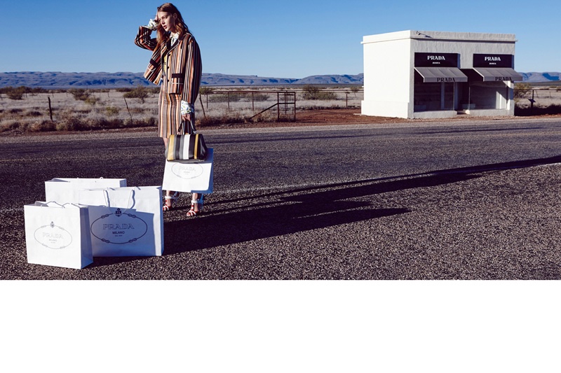 The model poses next to a Prada storefront wearing a striped jacket skirt, also from Prada
