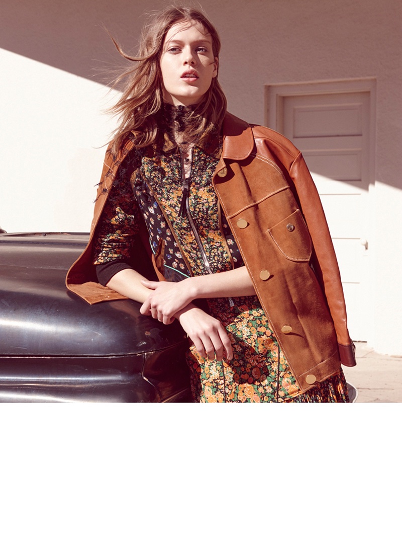 Posing next to a car, the model wears a brown jacket layered over a floral print dress