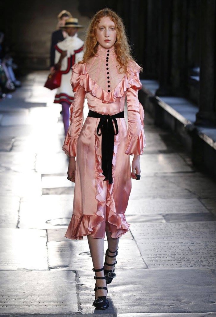 A model walks the runway at Gucci’s resort 2017 show wearing a pink dress with a high-neckline and ruffle details