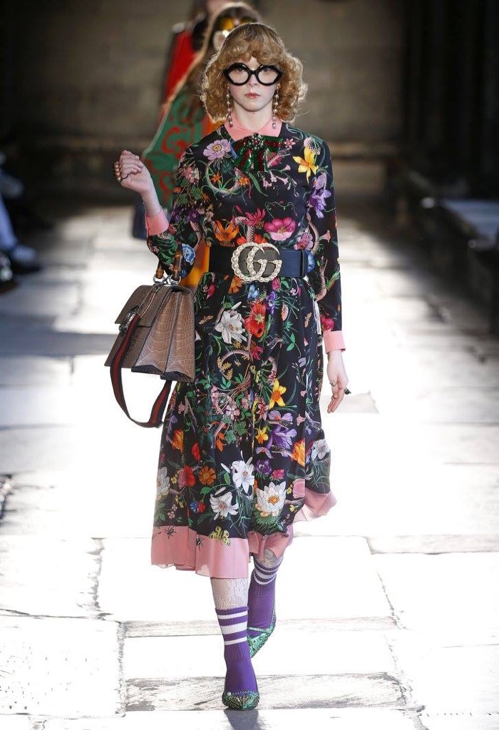 A model walks the runway at Gucci’s resort 2017 show wearing a floral print dress with a belt featuring the Gucci logo