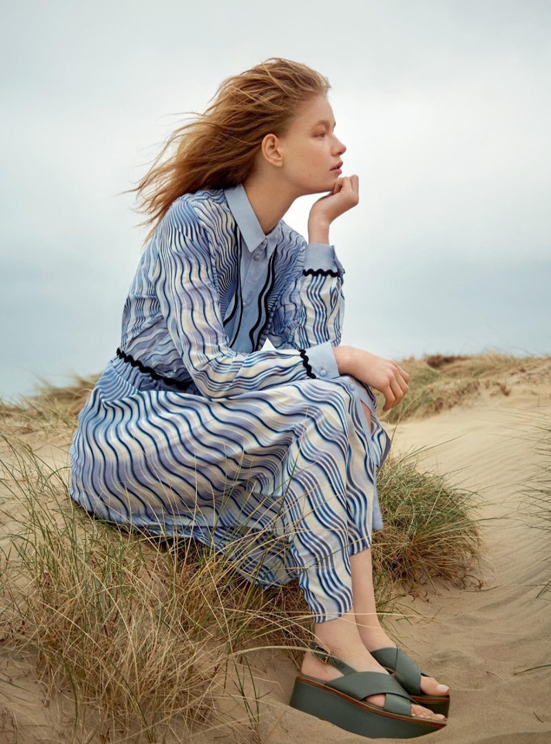 The model poses on the beach wearing a Mary Katrantzou printed dress