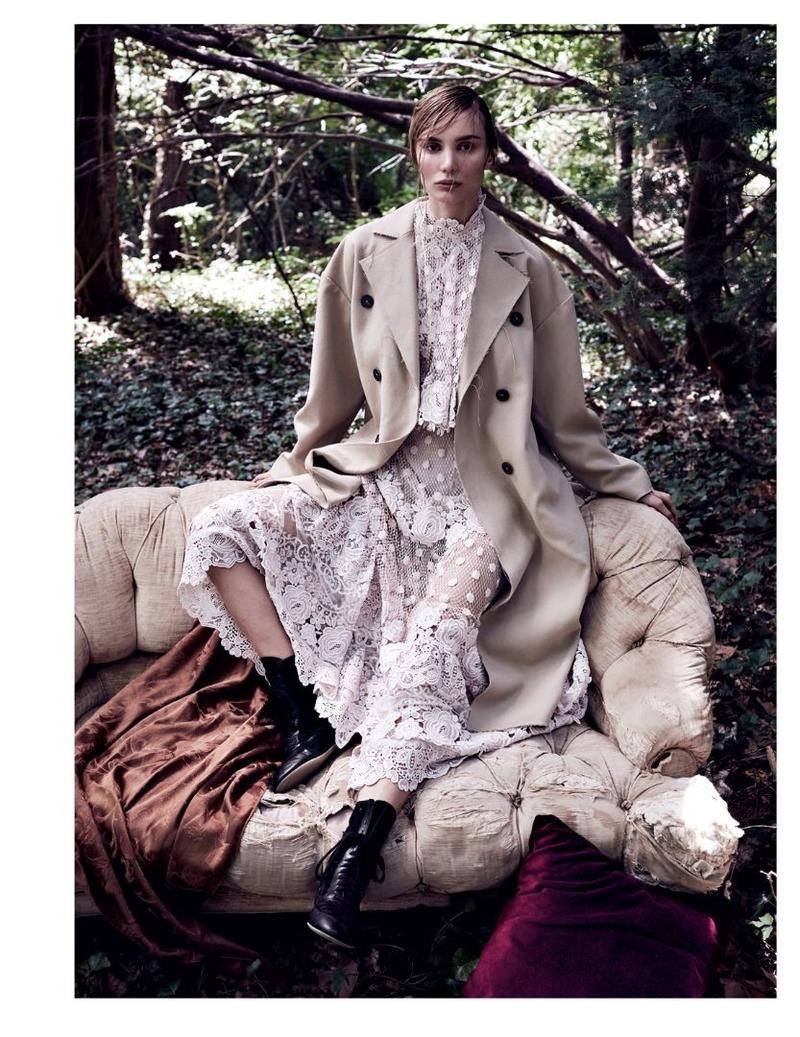 Sitting on a couch, Natalia Daragan poses in long coat and white maxi dress