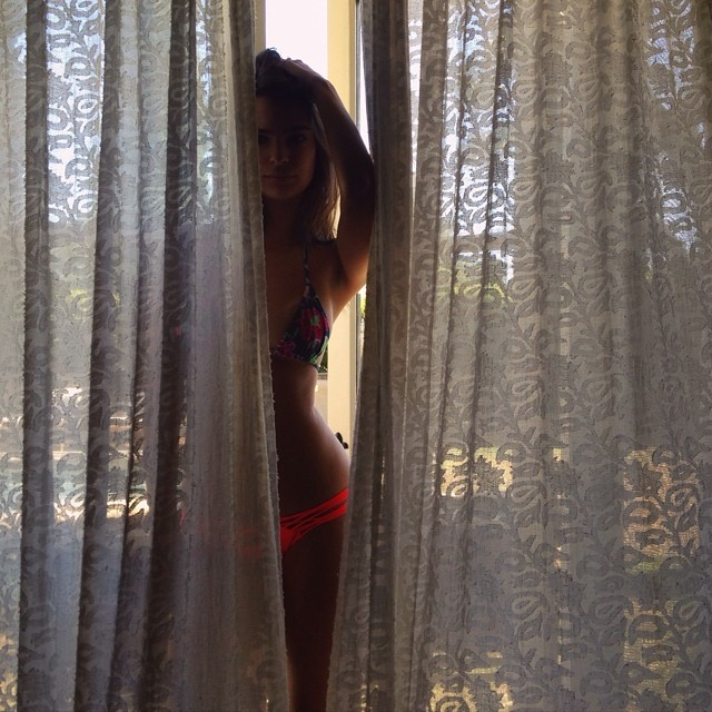 Emily Ratajkowski hides behind some sheer curtains in her swimsuit look