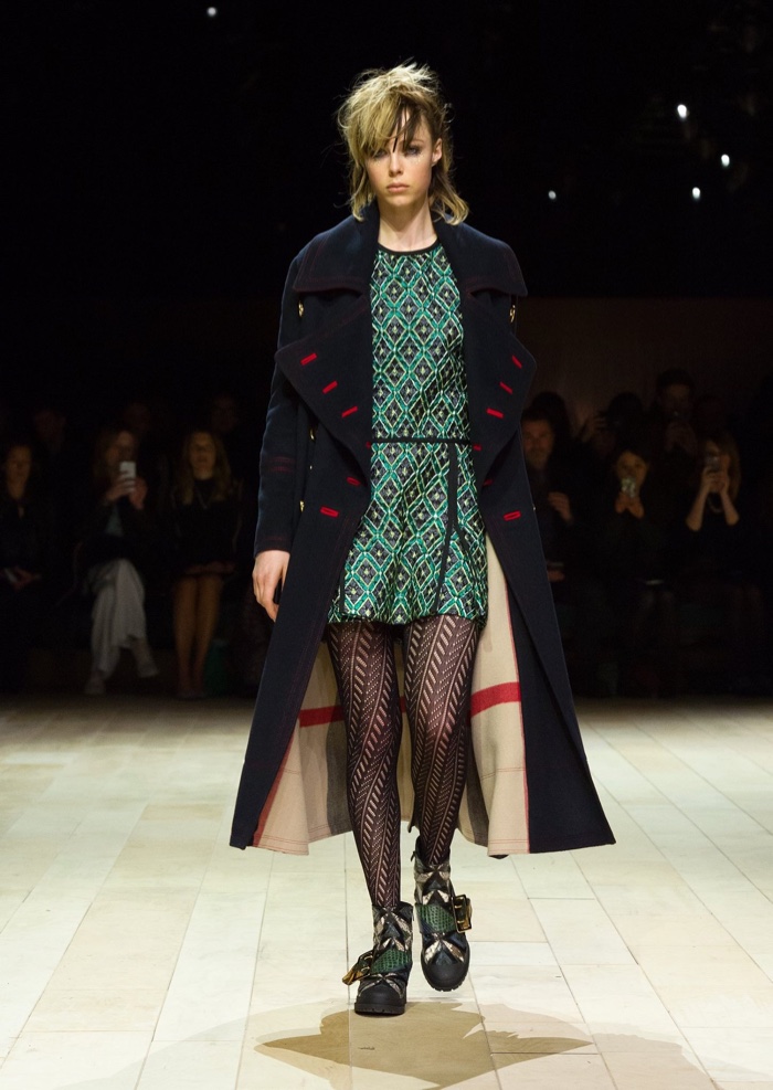 Edie Campbell walks the runway at Burberry’s fall-winter 2016 show wearing a military coat and metallic diamond jacquard pleated shirt dress