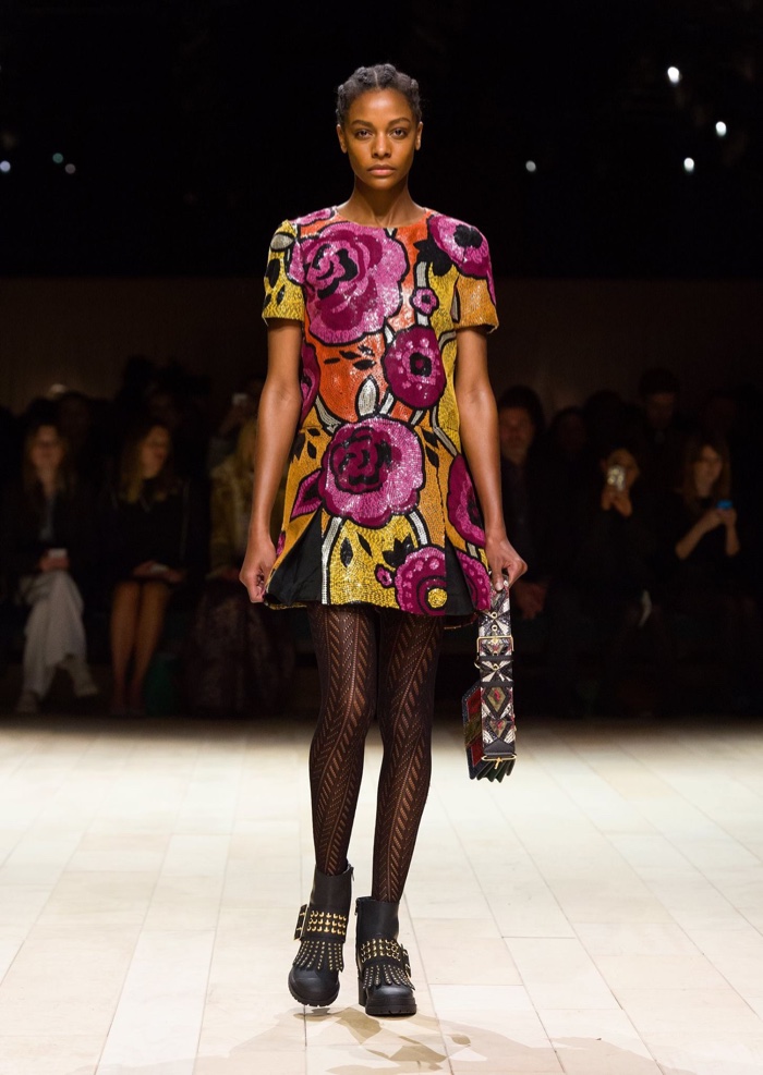 Karly Loyce walks the runway at Burberry’s fall-winter 2016 show wearing a sequin dress with floral print, Patchwork Bag and the Buckle Boot