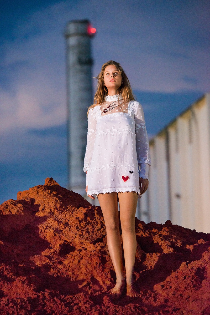 Anna Ewers poses outdoors in a high neckline white dress with long sleeves and hearts