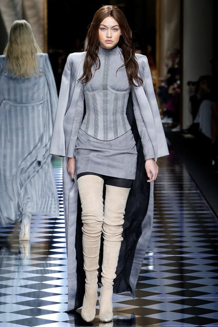 Gigi Hadid walks the runway at Balmain's fall-winter 2016 show wearing a brunette wig with a body-con dress, suede coat and thigh-high boots.