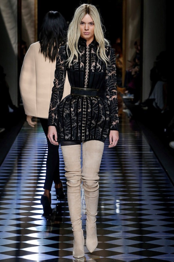 Kendall Jenner walks the runway at Balmain's fall-winter 2016 show wearing a black lace dress with padded hips and thigh-high suede boots