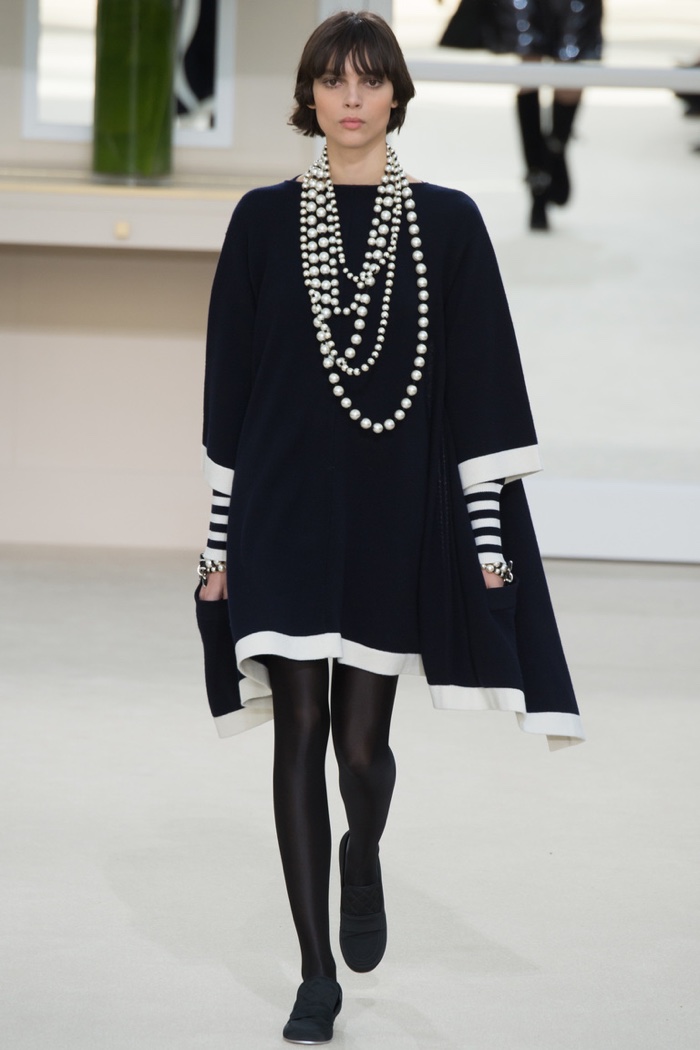 A model walks the runway at Chanel's fall-winter 2016 show wearing a black swing dress with layered pearl necklaces