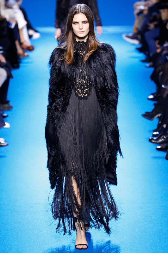 A model walks the runway at Elie Saab's fall-winter 2016 show wearing a fur coat with a fringe gown in black