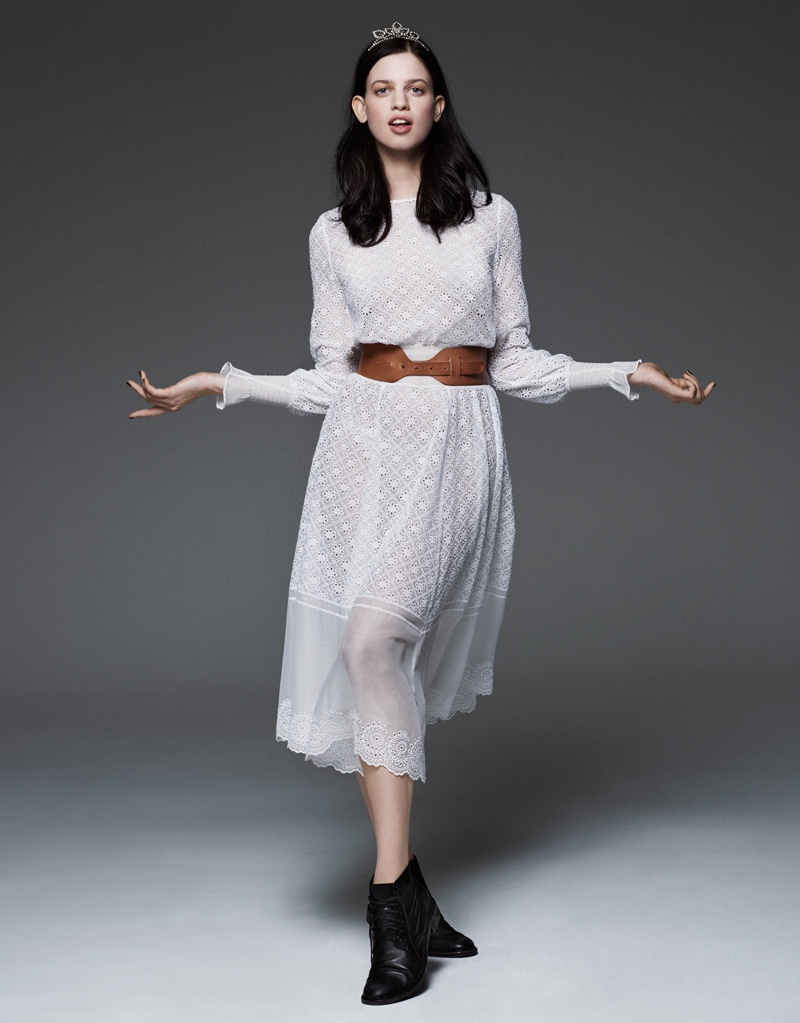 Posing in the studio, Lily wears a silver tiara and white long sleeve dress with ankle boots