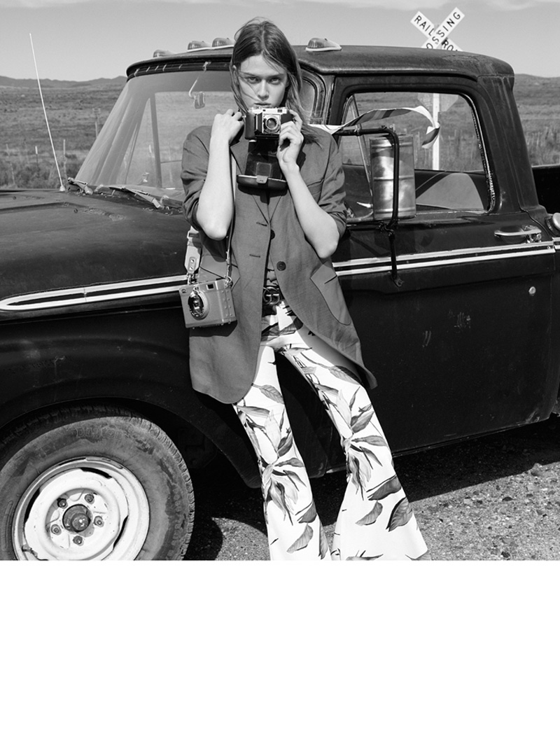 Posing with cameras, Tess wears long jacket and flared trousers