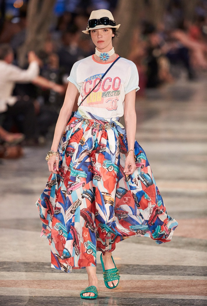 Mariacarla Boscono walks Chanel’s cruise 2017 show wearing a Panama hat, graphic t-shirt, car print skirt and embellished sandals