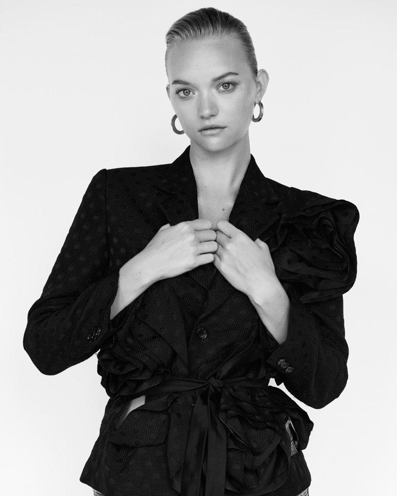 The blonde model poses in a jacket with broad shoulders cinched at the waist