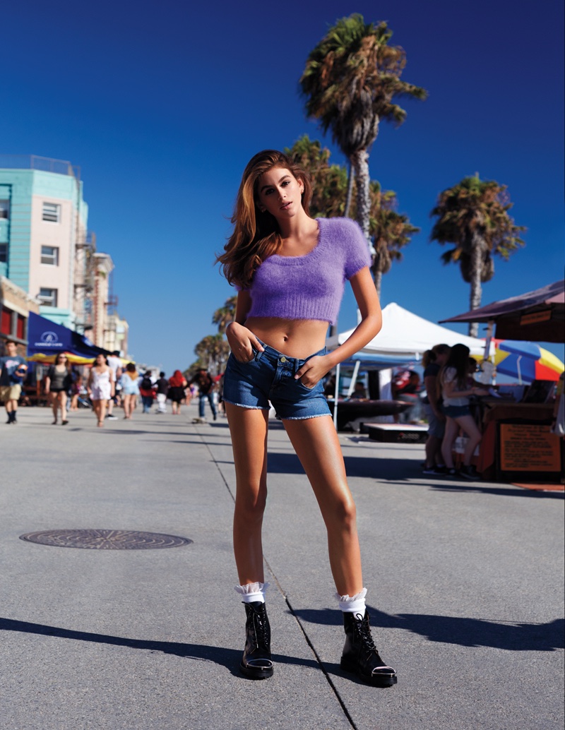 Kaia Gerber poses in Jeremy Scott cropped knit top with FRAME Denim shorts and Alexander Wang boots
