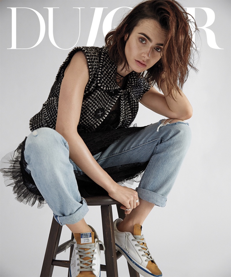 Sitting on a stool, Lily Collins poses in Dolce & Gabbana vest, Burberry dress, Levi’s jeans and Golden Goose Deluxe Brand sneakers