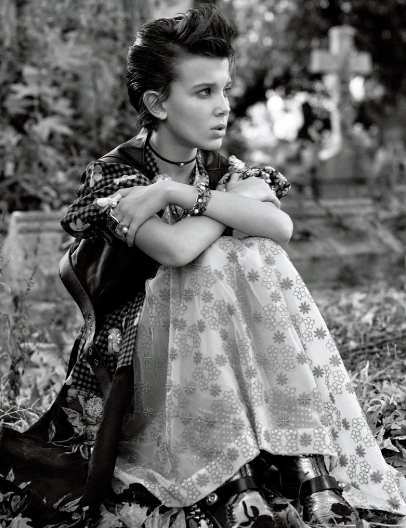 Sitting on grass, Millie Bobby Brown wears Coach vest with Simone Rocha dress