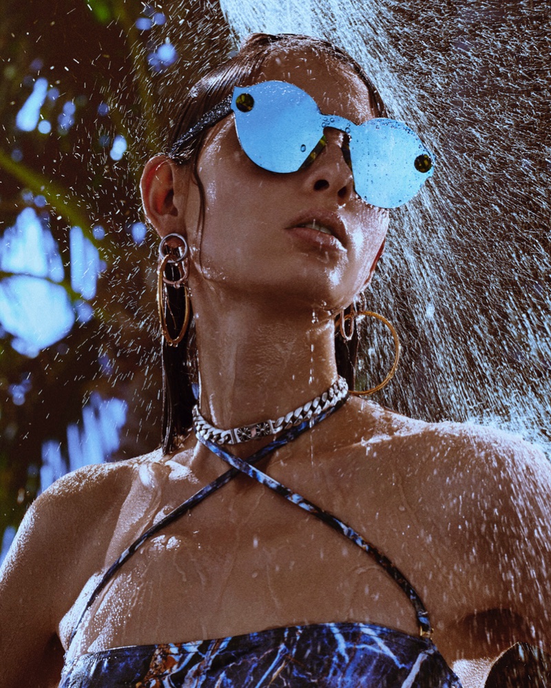 Model poses in Christopher Kane swimsuit and sunglasses with Alexander Wang earrings. Necklace by Chrome Hearts.