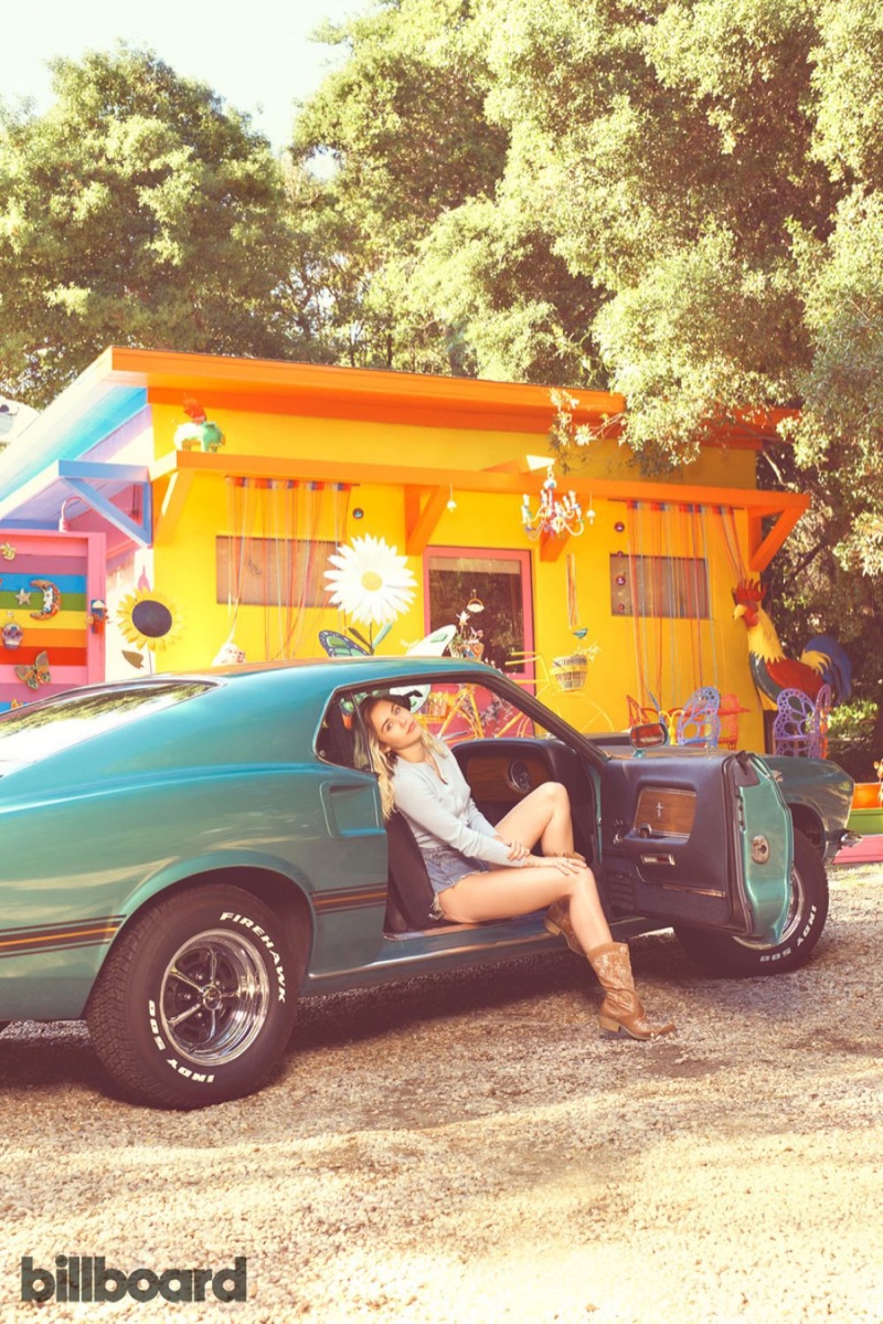 Sitting in a car, Miley Cyrus poses in long-sleeve t-shirt cutoff denim shorts