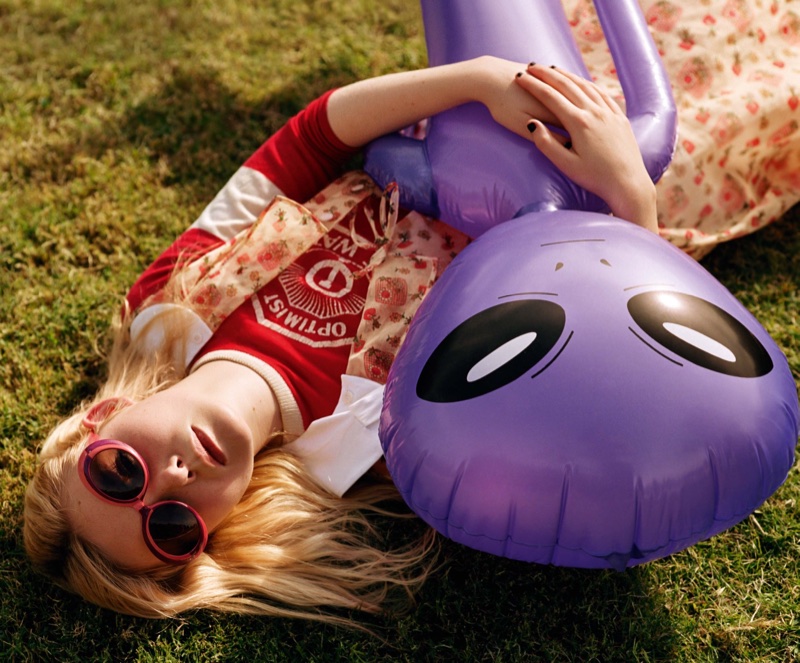 Posing on grass, Elle Fanning holds on to a purple alien toy