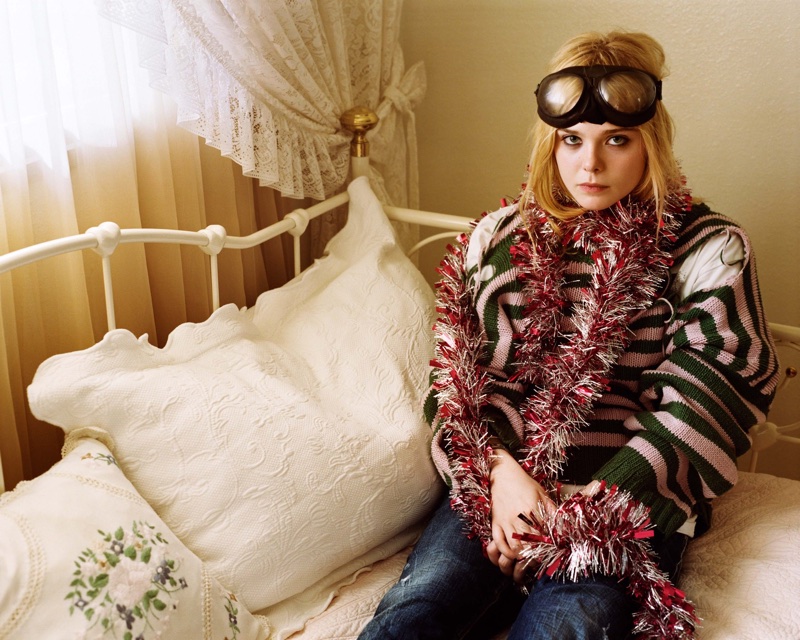 Posing in bed, Elle Fanning wears a whimsical look with a striped sweater