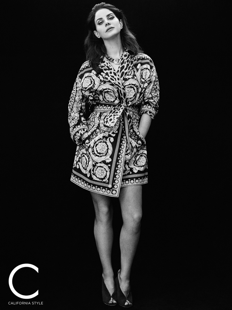 Photographed in black and white, Lana Del Rey wears Versace trench coat and choker necklace with Jimmy Choo heels