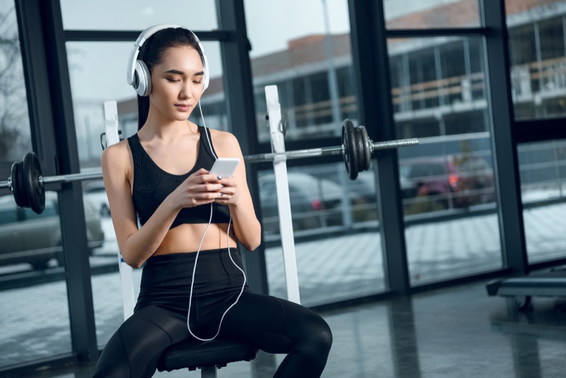 Attractive Asian Model with Phone Working Out at Gym