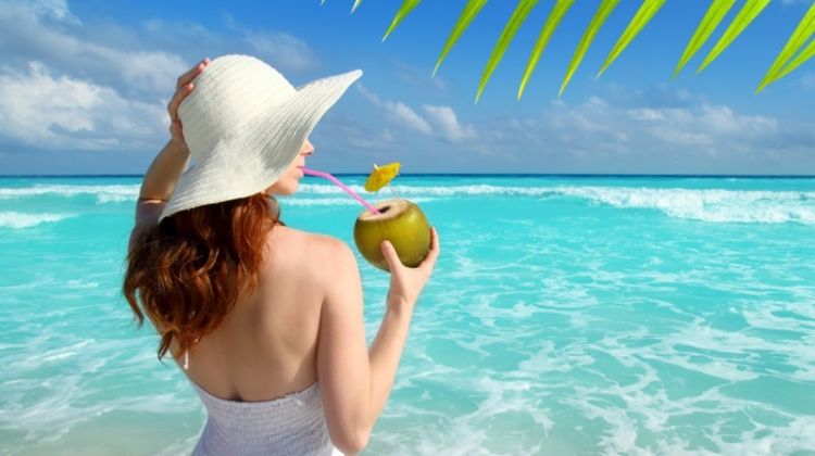 Our Favorite Destinations for a Warm Winter Getaway Woman Drinking Coconut Mexico Beach Hat White Dress