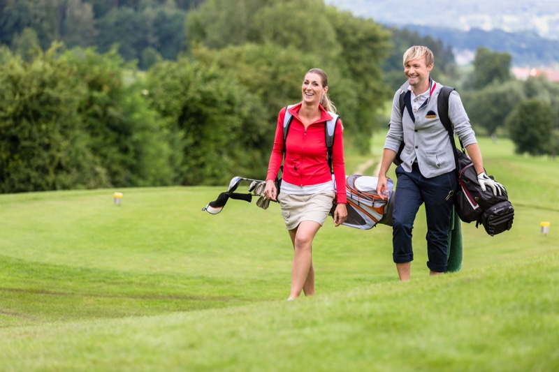 Couple Carrying Golf Bags Wearing Jackets Green