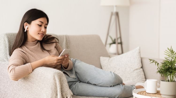 9 Extremely Useful Tips and Tricks for both New and Veteran AirPod Users Asian Woman Couch Airpods Lounging Phone