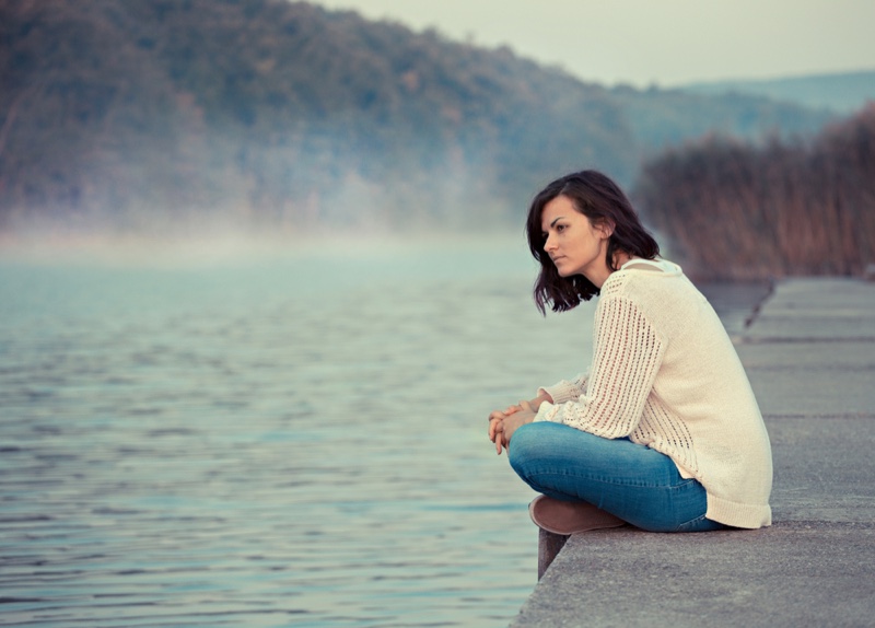 Brunette Woman Sitting Lake Water Sweater Jeans