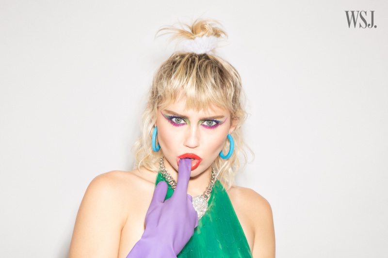Singer Miley Cyrus shows off a shimmering green top with purple gloves.