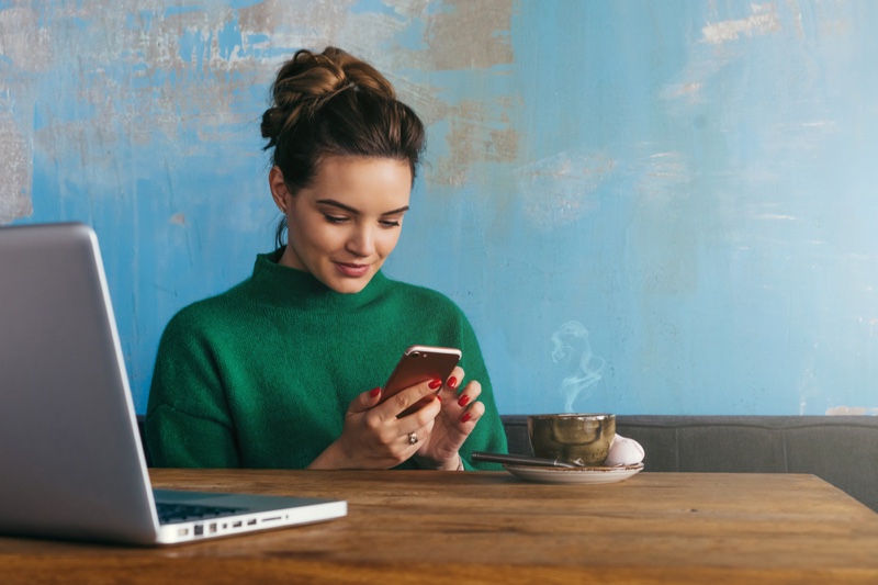 Brunette Woman Smiling Holding Phone Laptop Cup Table