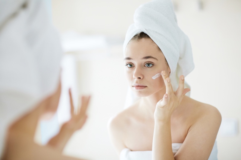 Young Woman Applying Cream Face Mirror