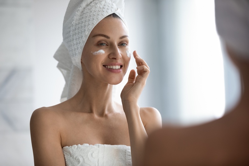 Woman Applying Face Cream Mirror Skincare Towel Cover Hair