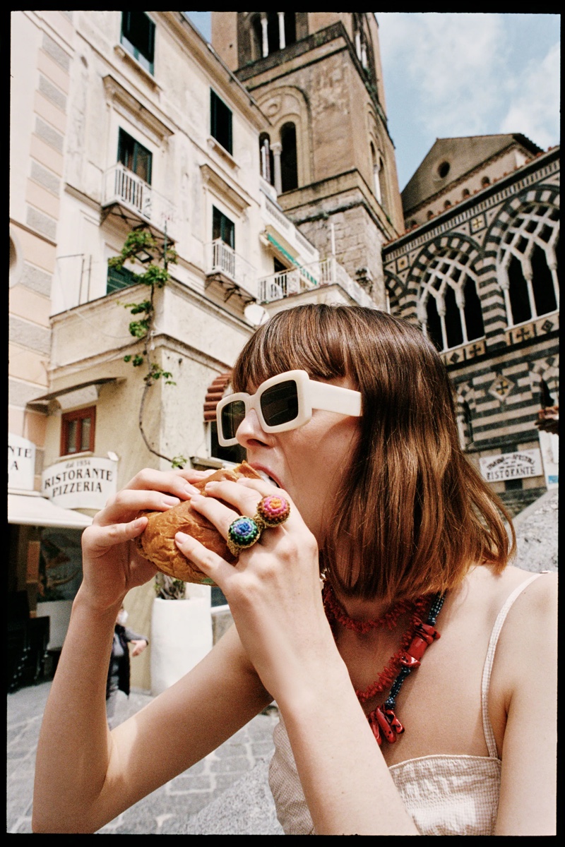 The model eats a hamburger with Zara's stylish sunglasses.