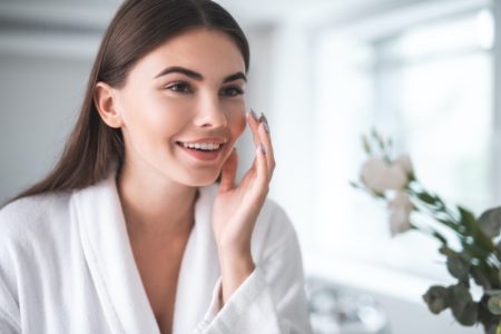 What Makes A Naturally Healthy Glow? Woman Touching Skin Mirror