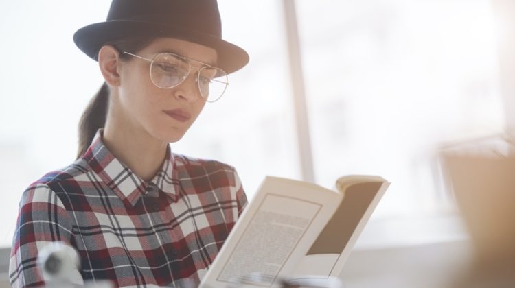 woman reading book aviator glasses plaid shirt hat