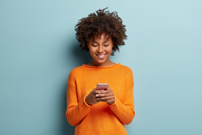 black woman natural hair orange sweater phone smiling