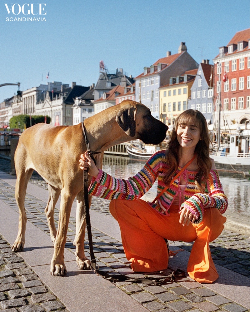 Modeling with a dog, Lily Collins wears an orange outfit.