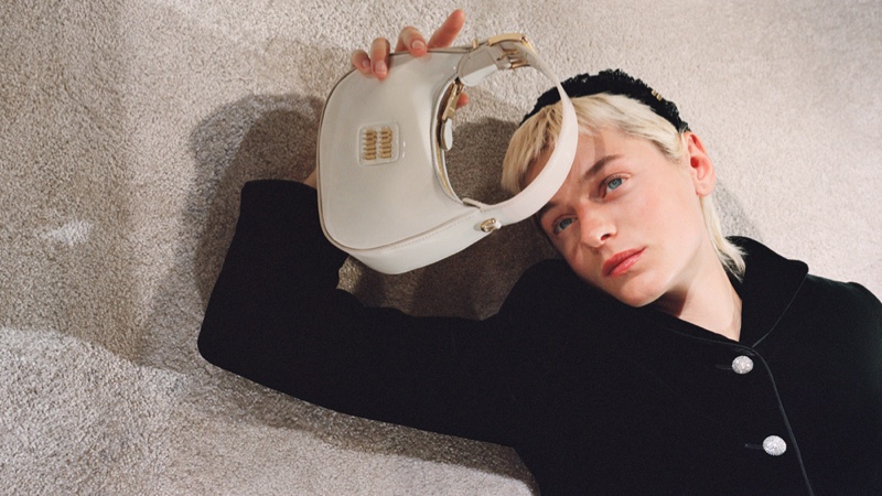 Posing with a shoulder bag and headband, Emma Corrin fronts Miu Miu's holiday 2023 advertisements.