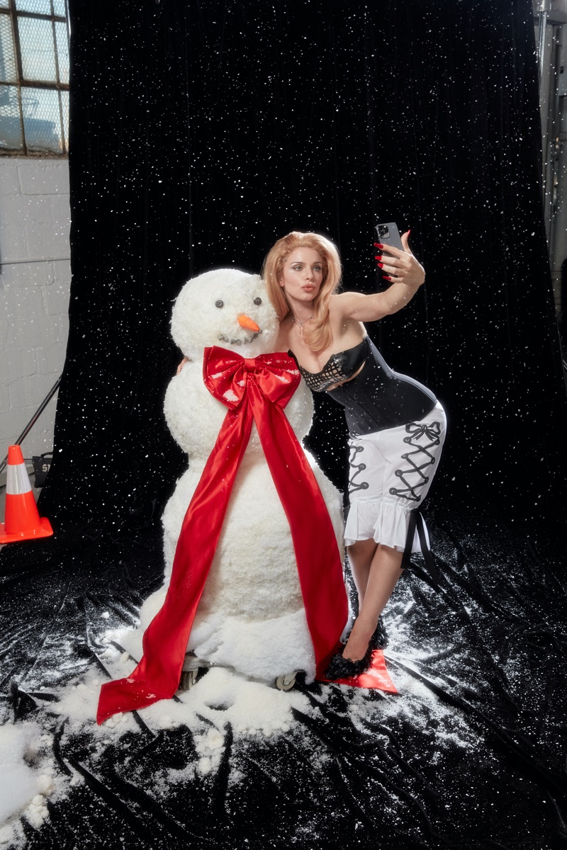 Posing next to a snowman, Julia Fox wears glamorous corset-style dress with lace-up details for SSENSE holiday 2023 guide.