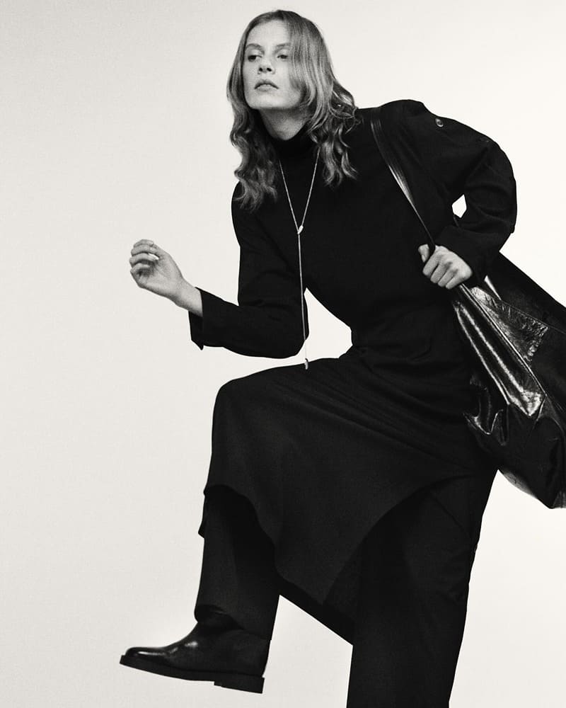 Massimo Dutti exudes dynamic elegance with a sleek all-black outfit featuring a turtleneck, flowing trousers, and boots.