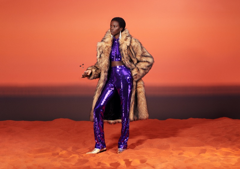 Anok Yai shines in purple crop top and pants with faux fur coat for Rabanne and H&M's collaboration campaign.