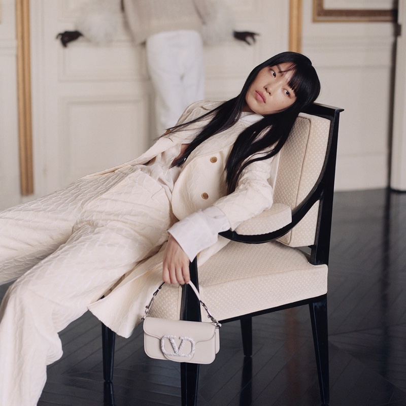 Gao Jie lounges in a textured Valentino suit, pairing it with a handbag, for the brand's holiday 2023 campaign.