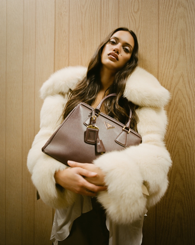 Dalianah Arekion accentuates luxury in a plush white fur coat, clasping an elegant Prada handbag for WGACA's holiday 2023 campaign.