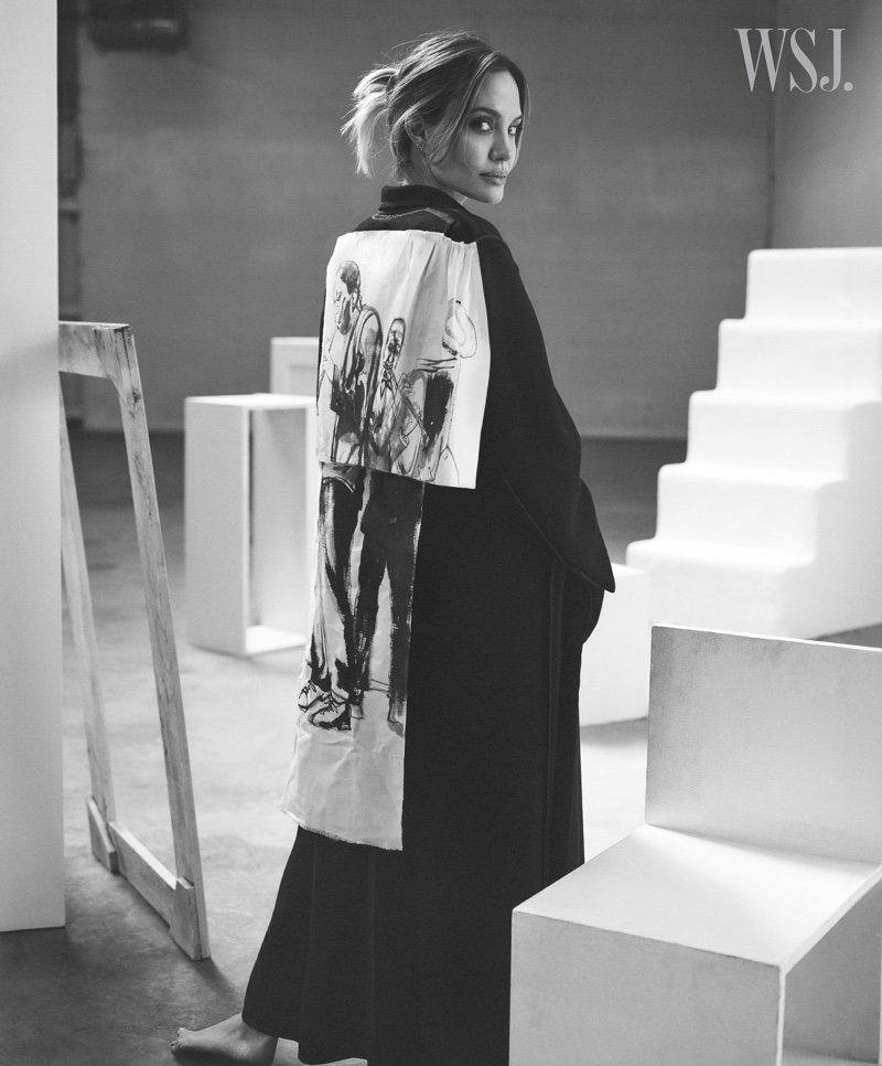 Angelina Jolie stands out against the stark lines of an abstract setting, draped in a cape with striking graphic detail.