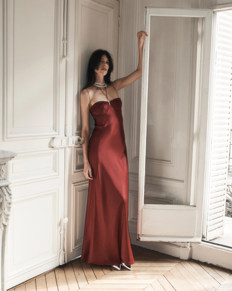 A model poses in a classic red bustier slip dress from the Anna October x J. Crew holiday 2023 collection, embodying timeless grace.