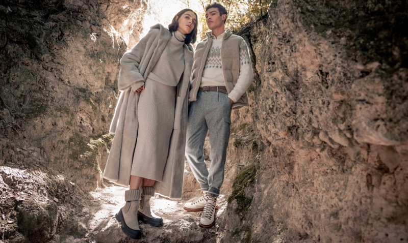 Amidst a rocky alcove, a duo models Brunello Cucinelli's boots and sneakers, showcasing the versatile elegance of the fall-winter collection.